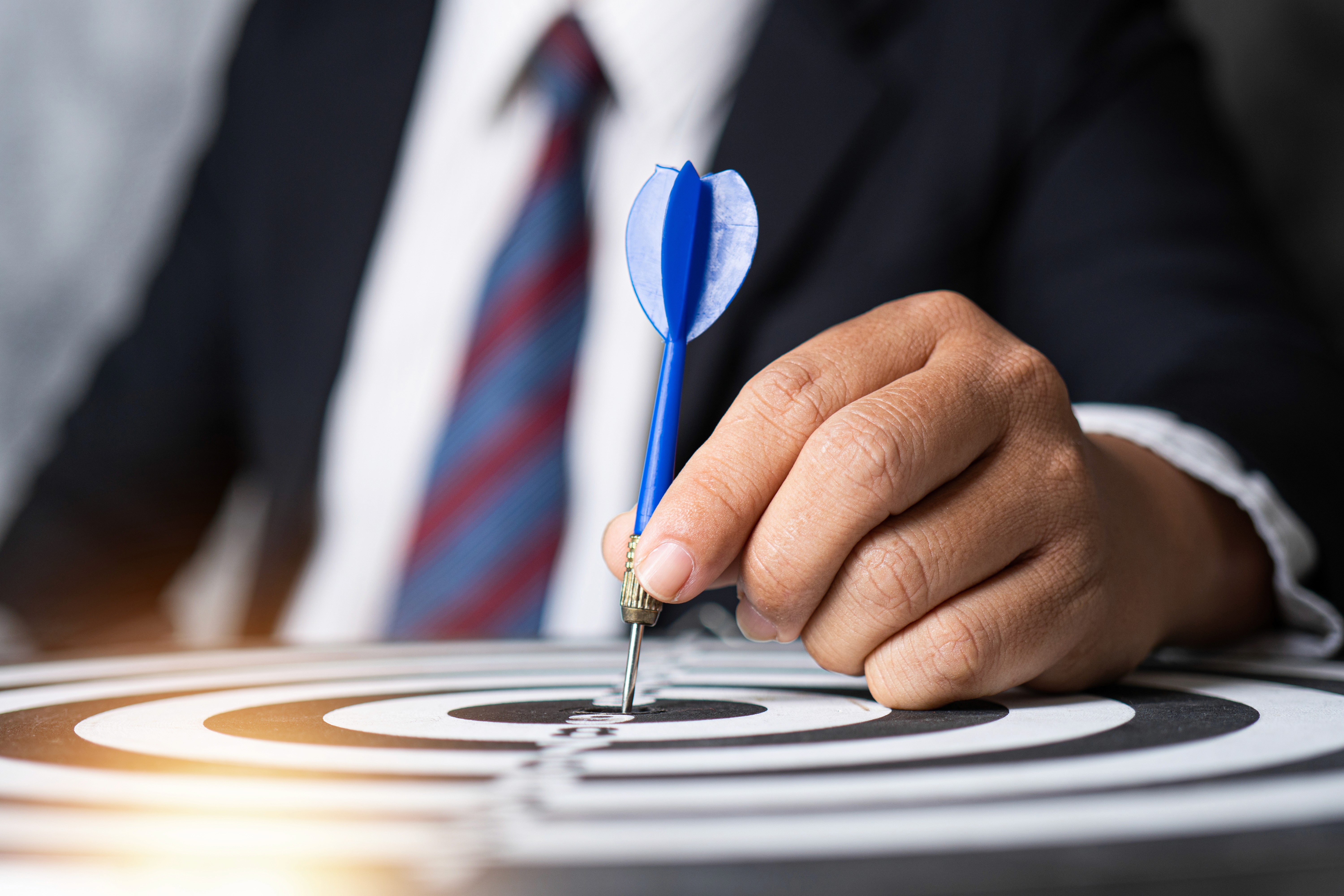 A young person with curly hair smiles at the camera while sitting in front of a laptop against a dark background.