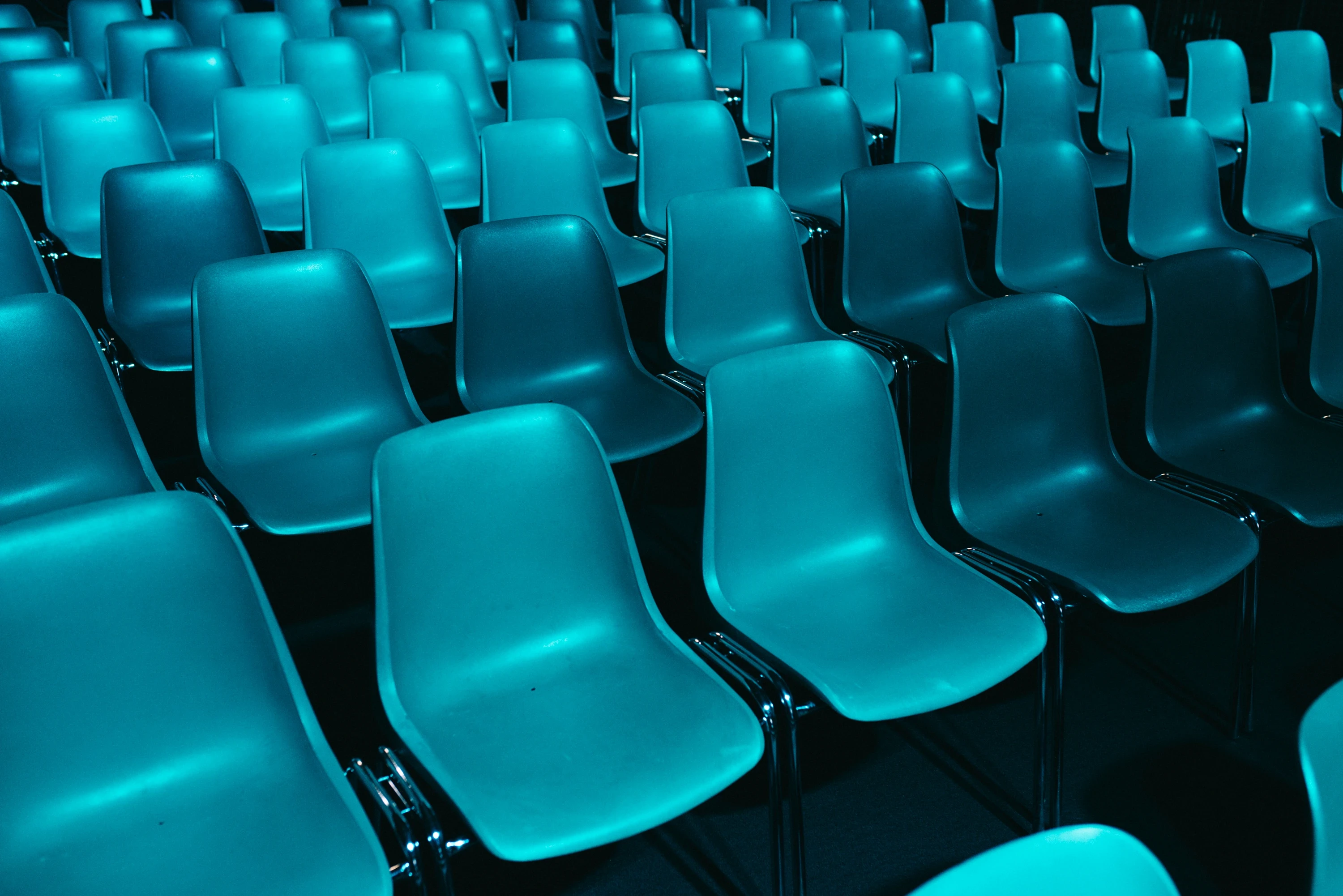 Rows of turquoise-lit shell chairs for the FASHIONTECH Berlin conference.