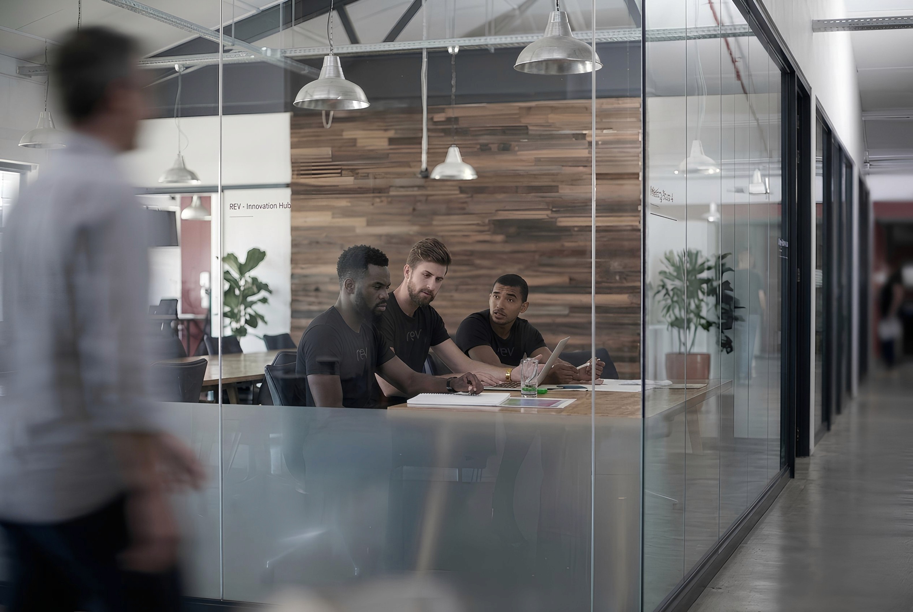 Spacious modern open-plan office with floor-to-ceiling windows, monitor workstations, and greenery