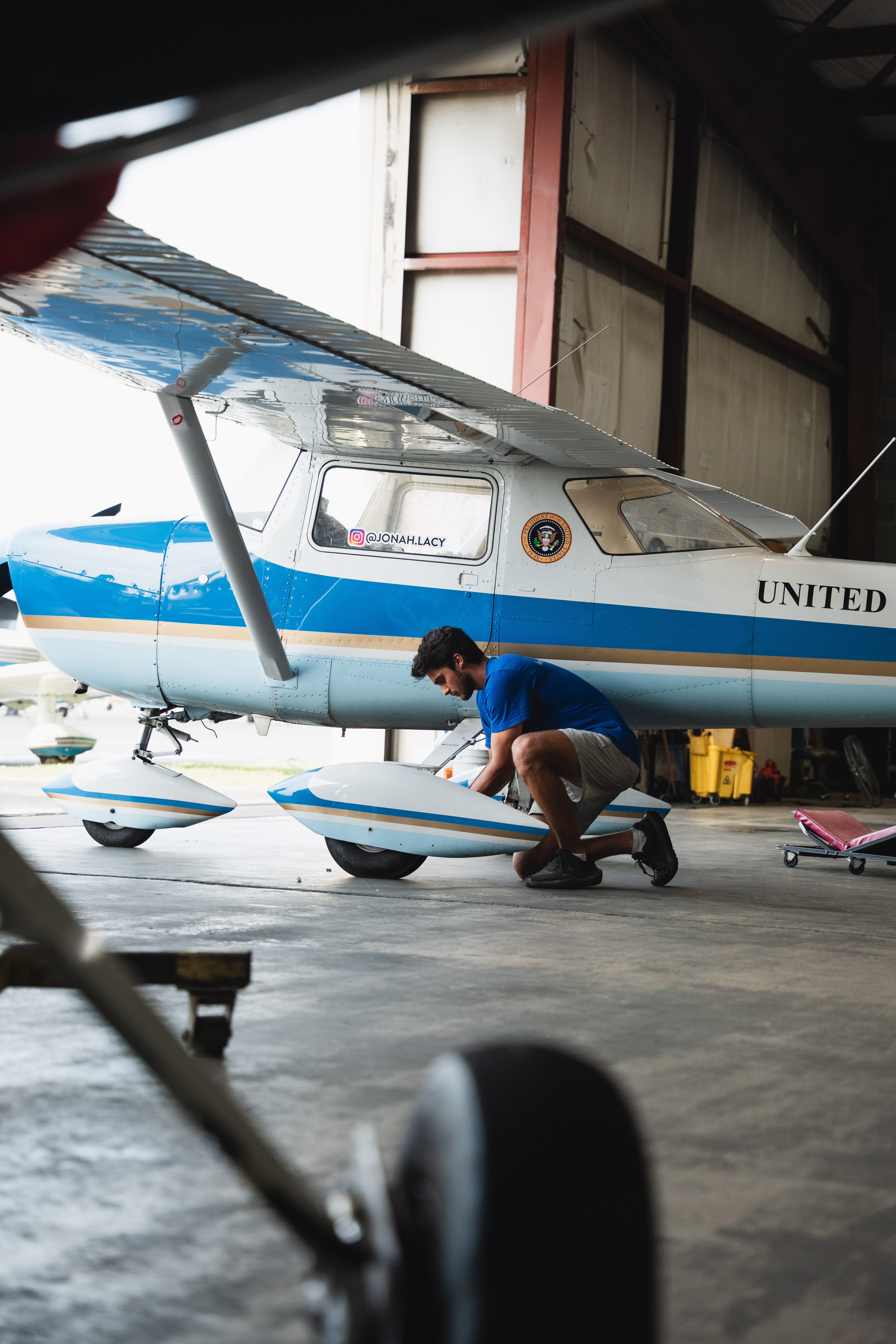 Smiling man wearing a cream sweater sitting against a wooden background.