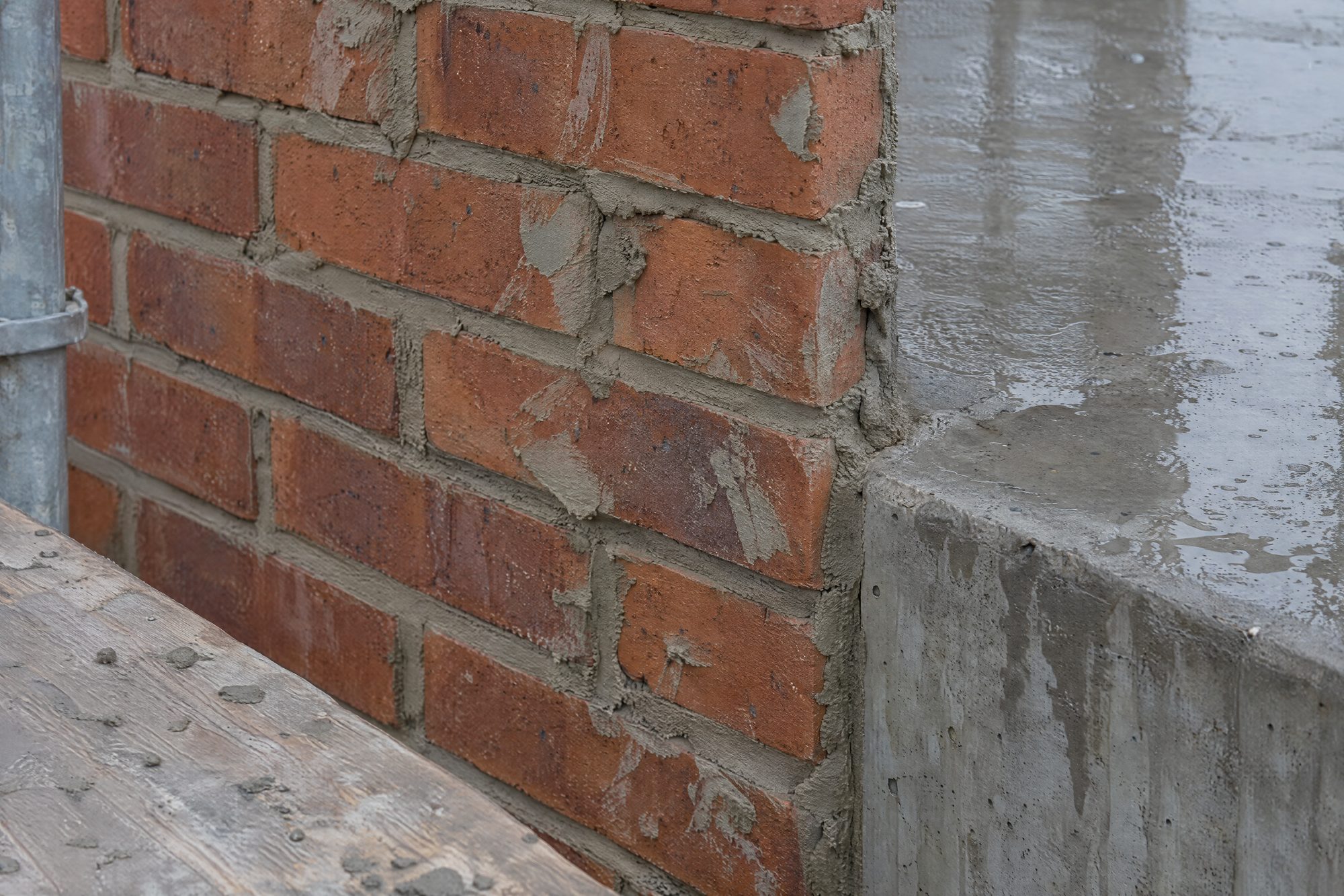 New brickwork beside a wet concrete edge, the mortar not yet cleaned off
