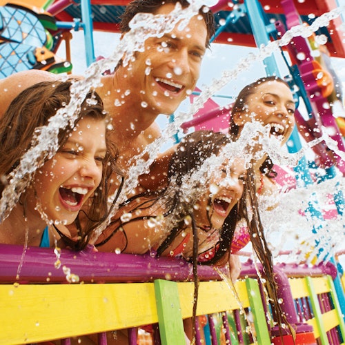 Четирима души се смеят и ги опръсква вода на цветна атракция в увеселителен парк.