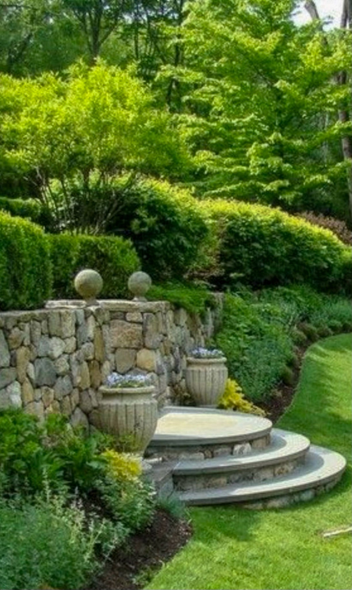 Curved stone garden steps with urn planters and layered plantings