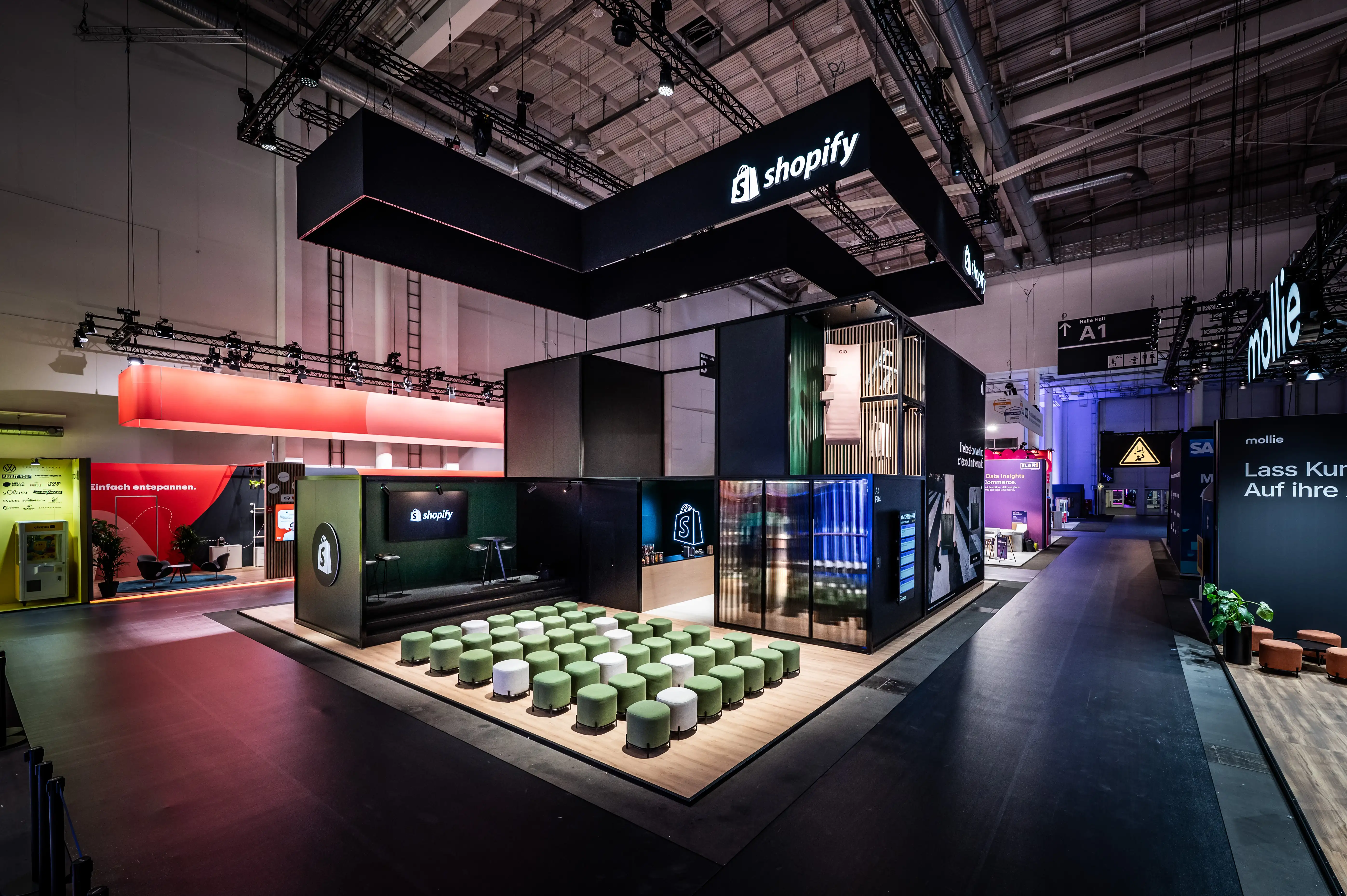 Shopify booth with green stool seating in front of the stage and glass cube rooms in the hall.