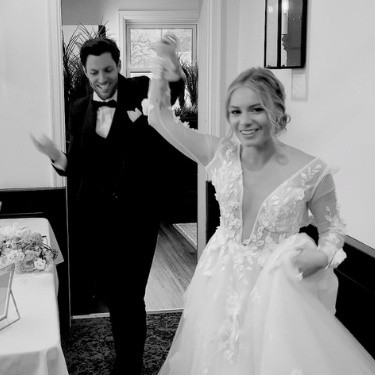 The bride and groom making a grand entrance at their wedding reception, walking hand-in-hand to cheers and applause from their excited guests.