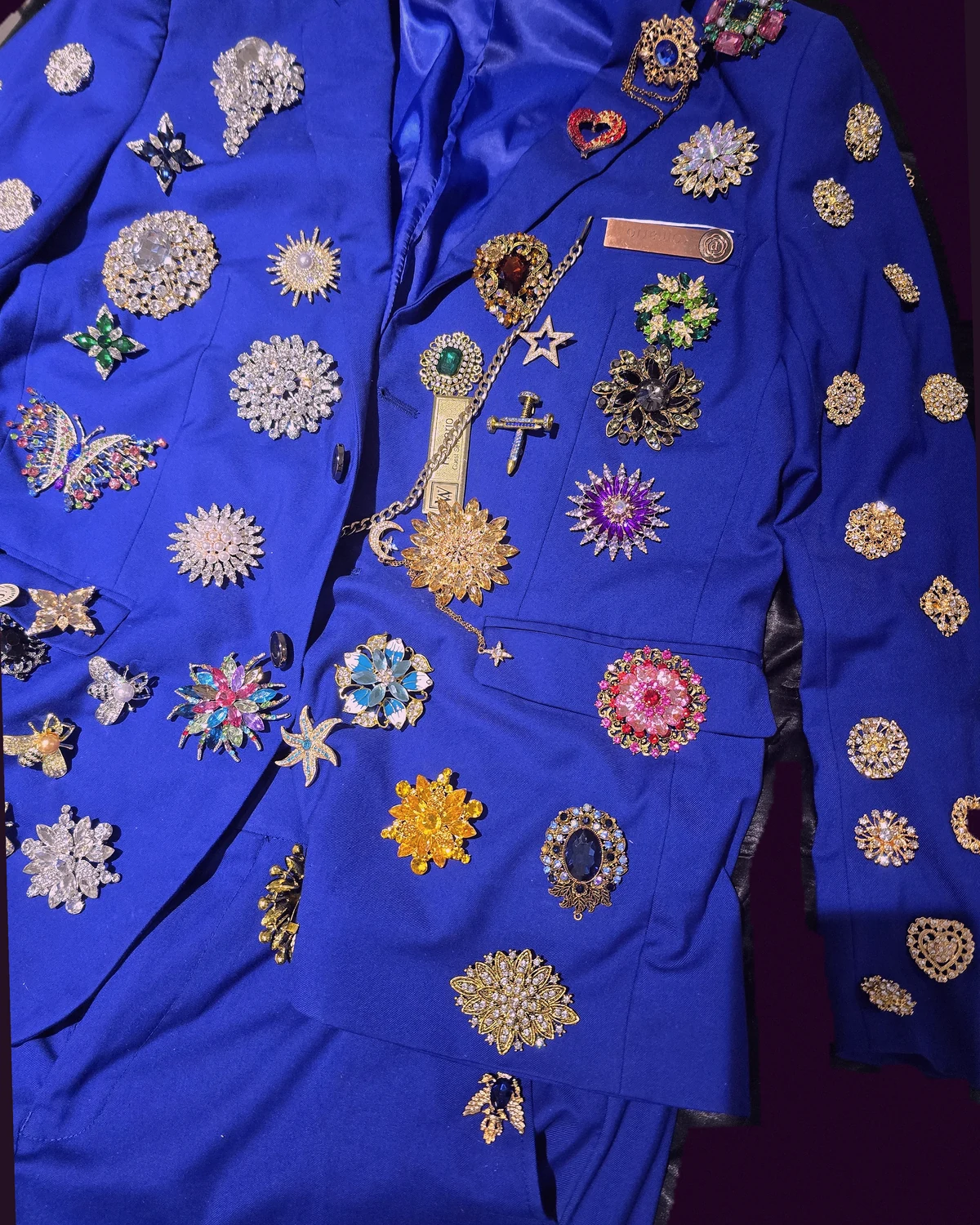 Wonder Suit jacket detail with its original brooches under a pink and cobalt Japan-inspired color grade.