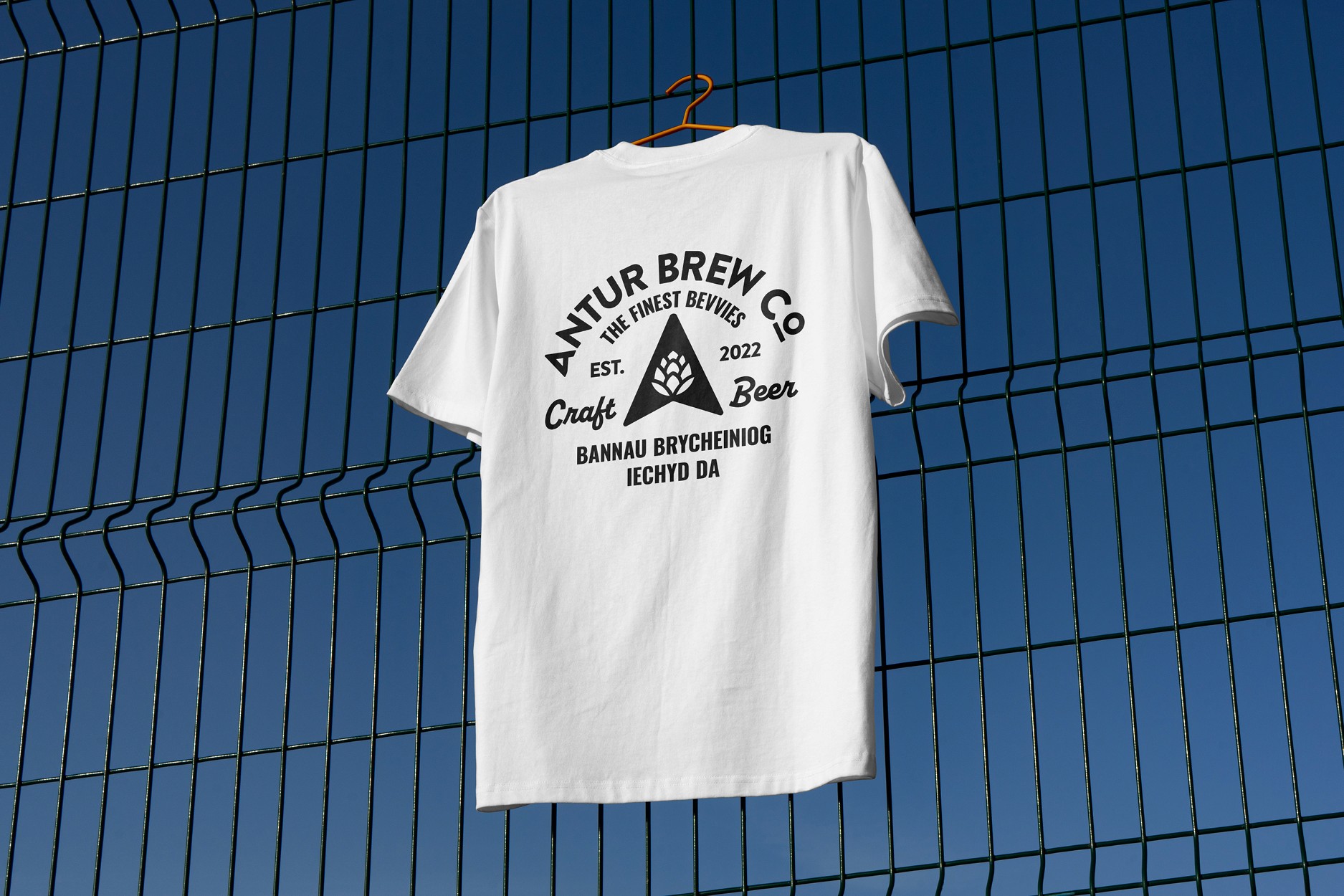 White Antur Brew Co T-shirt hanging on a fence, featuring black graphic text and logo design including ‘The Finest Bevvies’ and ‘Craft Beer’.