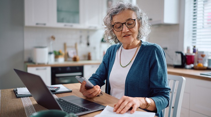 Older lady sitting at a kitchen table with a phone and laptop