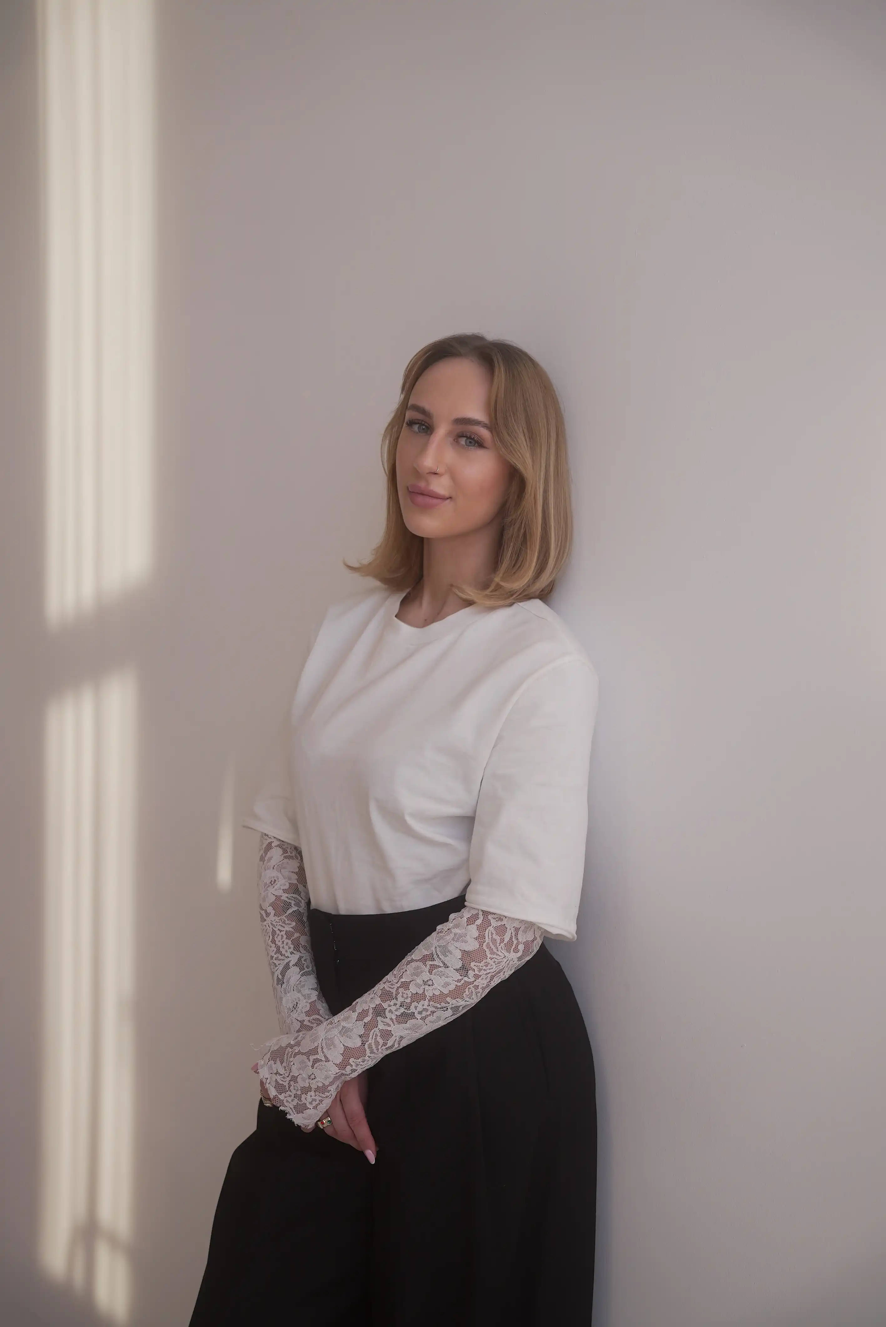 Blondynka w białym ubraniu opiera się o ścianę