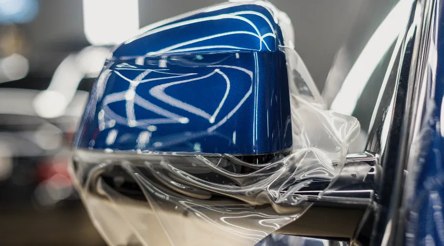Blue car side mirror with clear protective wrap.