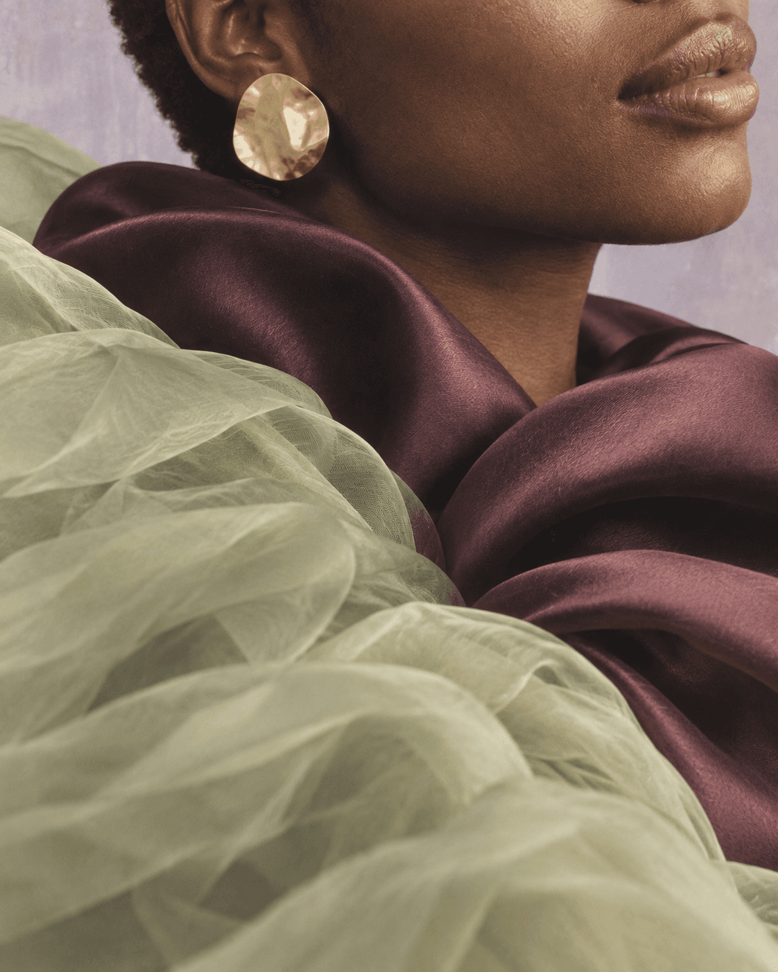 Close detail of hammered gold, warm skin and sculptural plum satin folds.