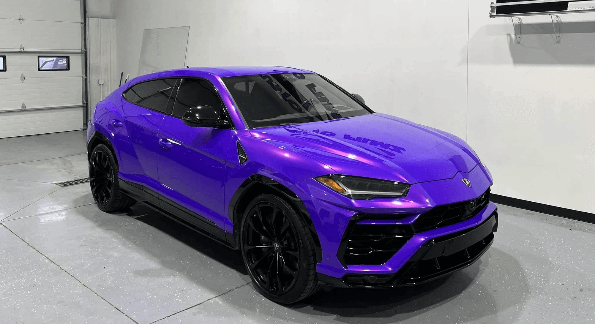 A vibrant purple Lamborghini Urus is parked indoors on a polished concrete floor.
