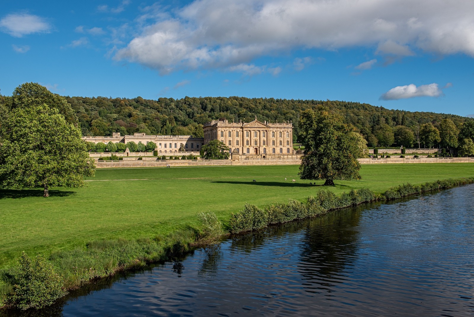 Chatsworth House set within expansive parkland beside a calm river, symbolising heritage, governance, and multi-generational continuity.