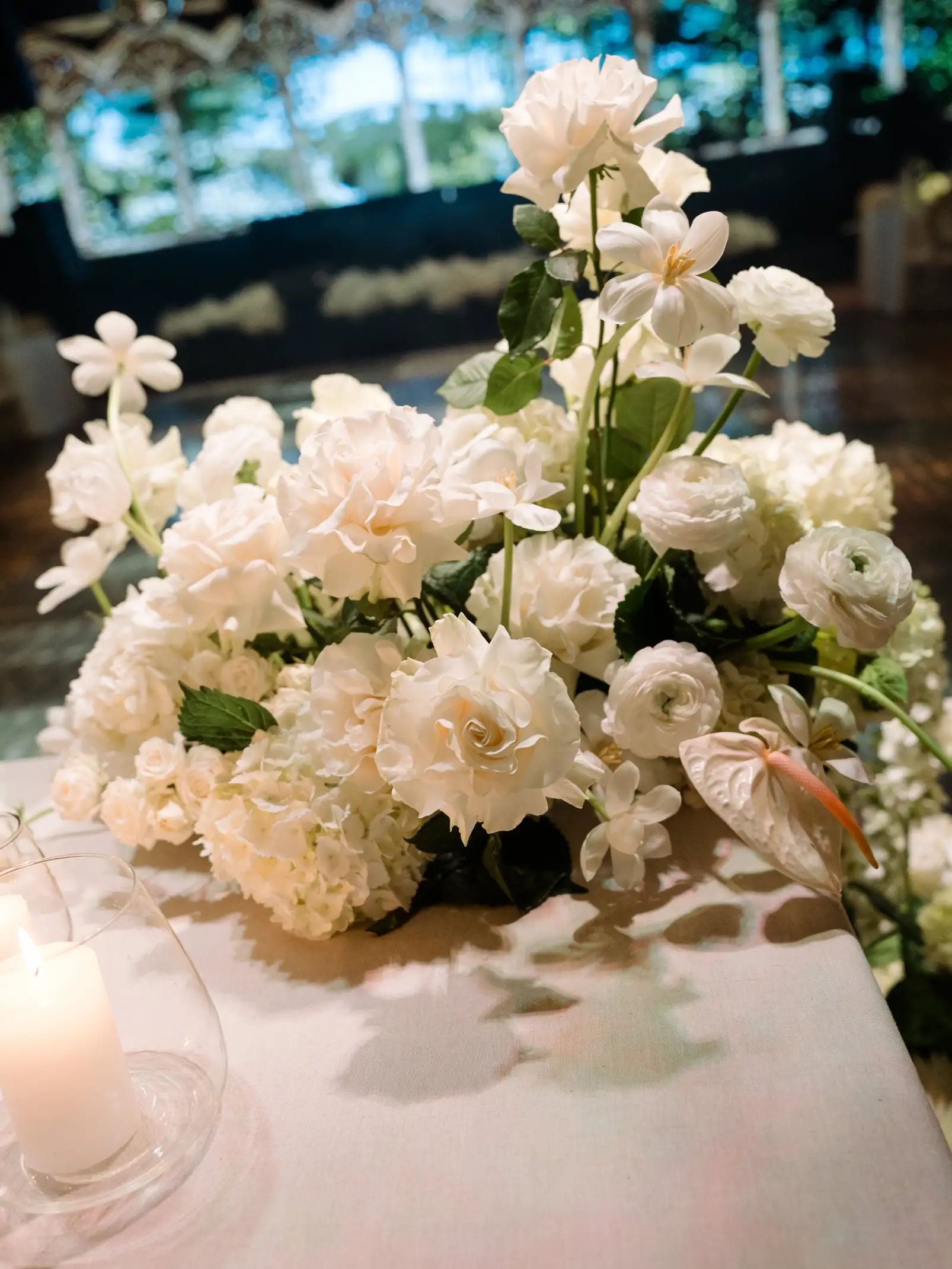Arreglo floral blanco con rosas, anthuriums y velas, destacando la pureza y el equilibrio del diseño.