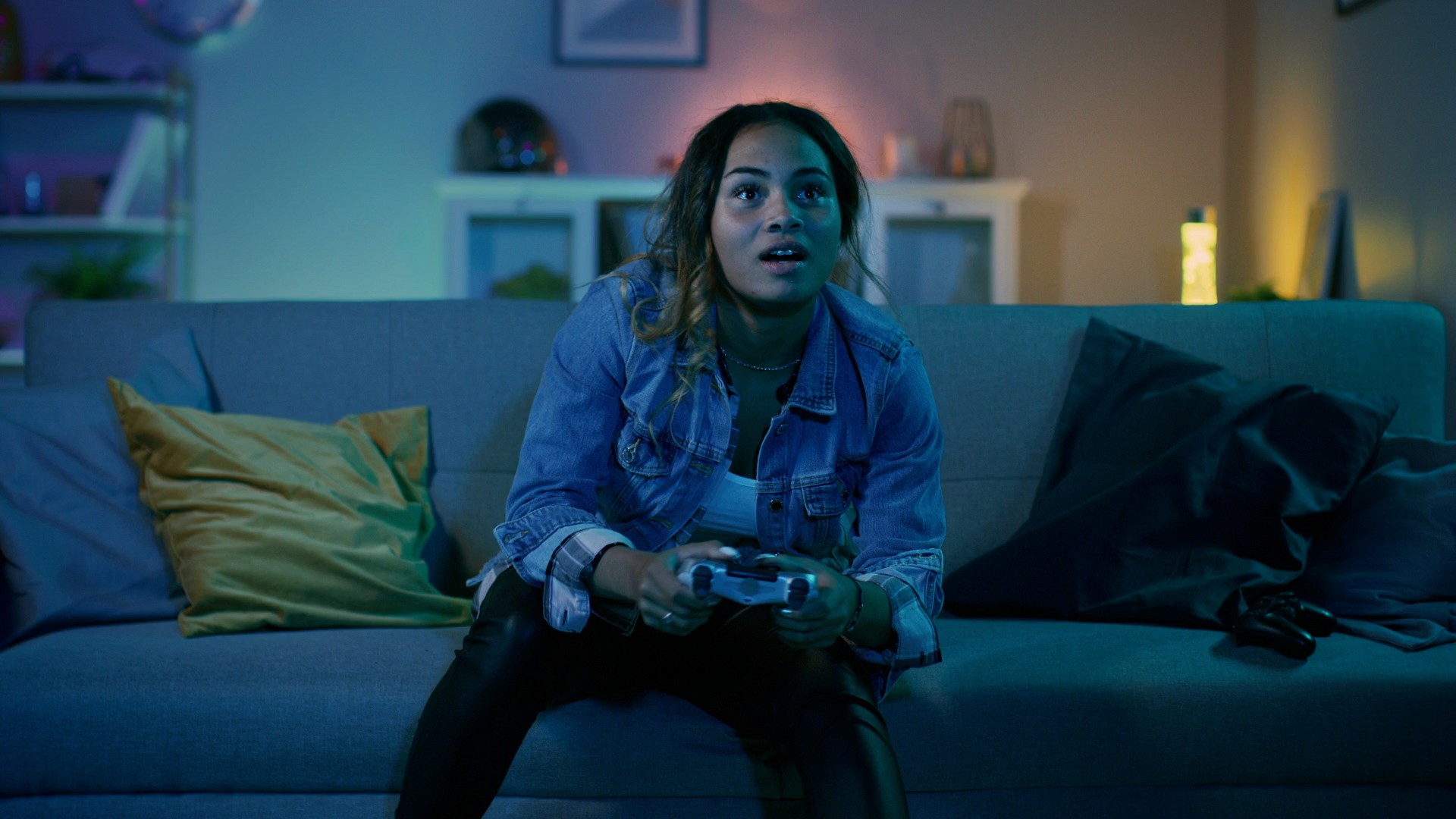 Young woman gaming with PlayStation controller in cozy room, representing PlayStation Plus – Are You Player? microsite by Burak Canpolat.