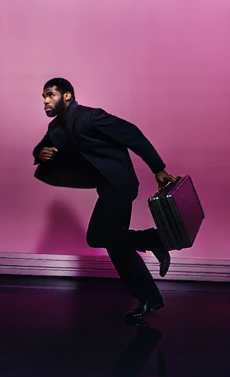 Studio-style image of a man in a black suit running with a metal briefcase against a magenta backdrop