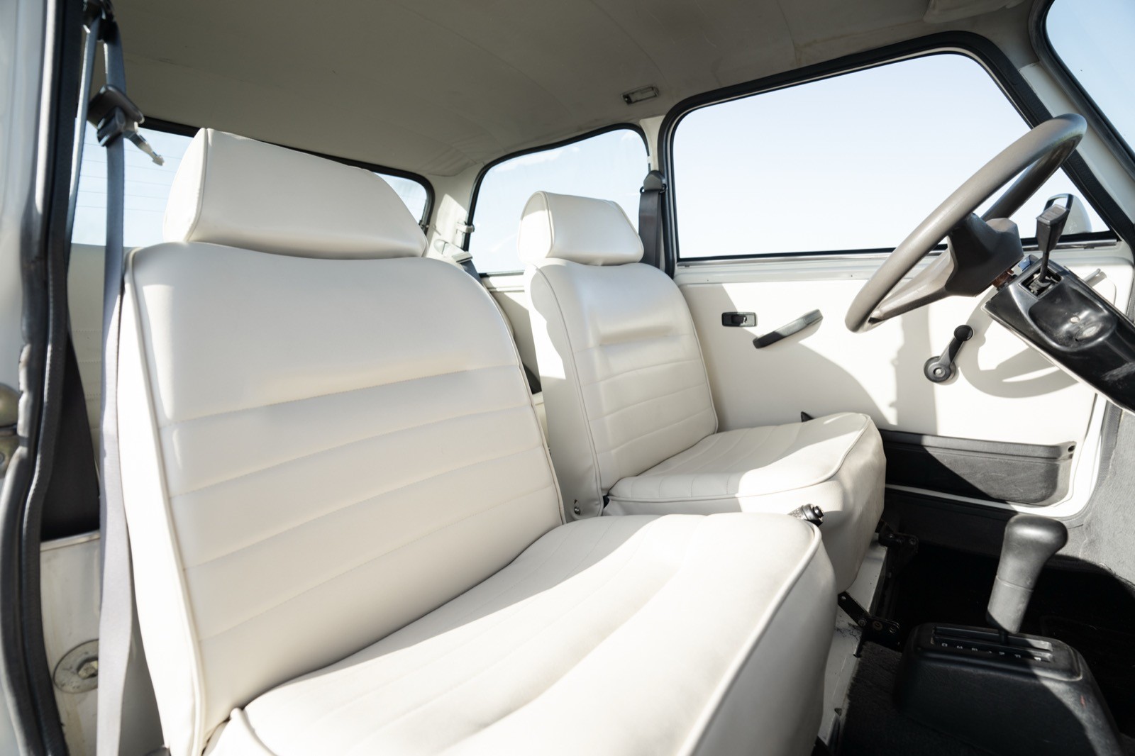 Interior of a vehicle featuring two white seats and a steering wheel, with a blurred outdoor view through the windshield.