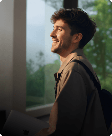 Become a channel partner - Happy man with a backpack holding a laptop looking out a window into the greenery.