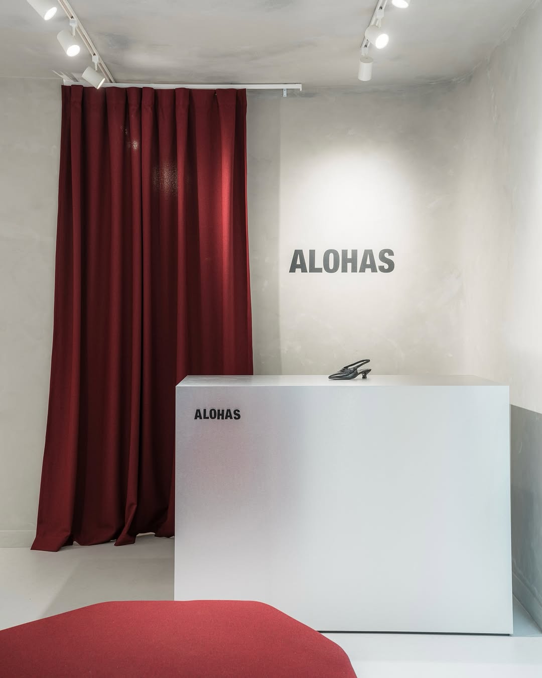 Reception area inside the Alohas New York retail store featuring minimalist logo signage on the desk and wall, set against soft plaster finishes and deep red curtains.