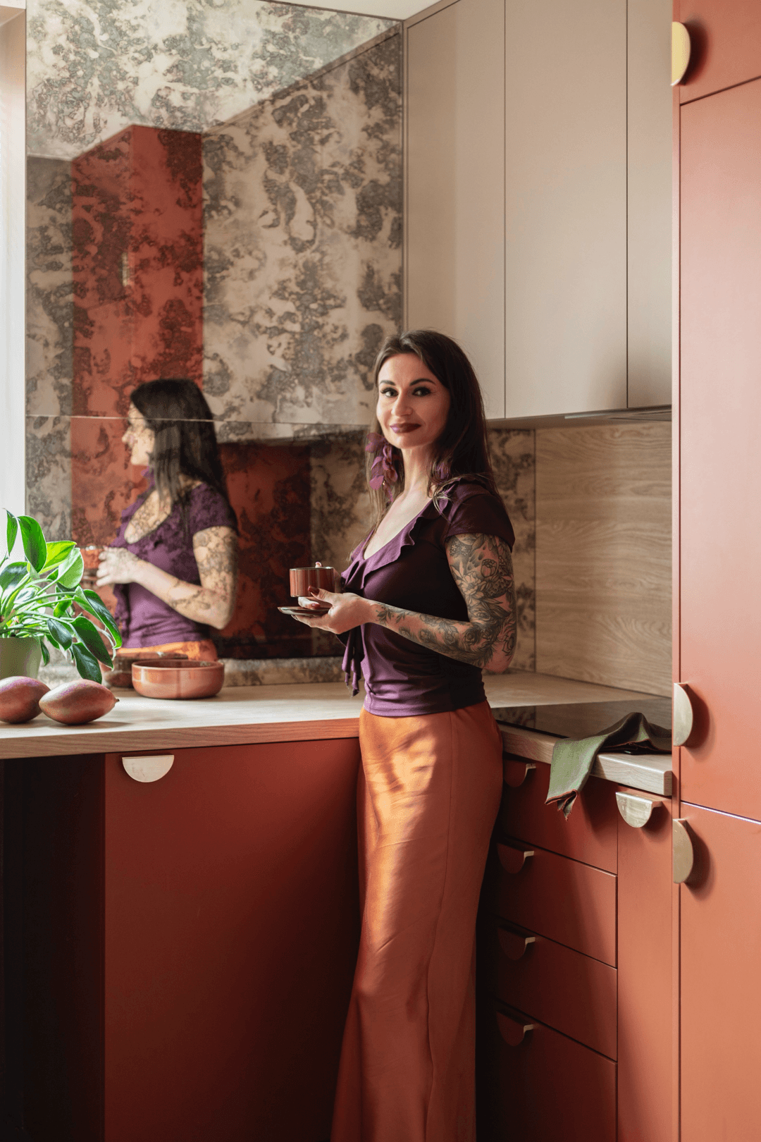 Projektantka w bordowej sukience siedzi na kanapie w otoczeniu roślin.