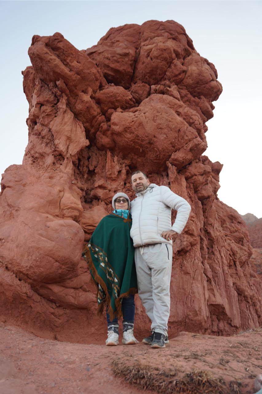 Mujer sentada sobre un tronco frente a una cascada doble en un bosque frondoso de Argentina.