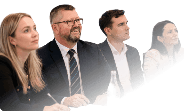 A group of business professionals sitting together and listening attentively during a seminar or panel discussion, presented with a dark teal graphic background overlay.
