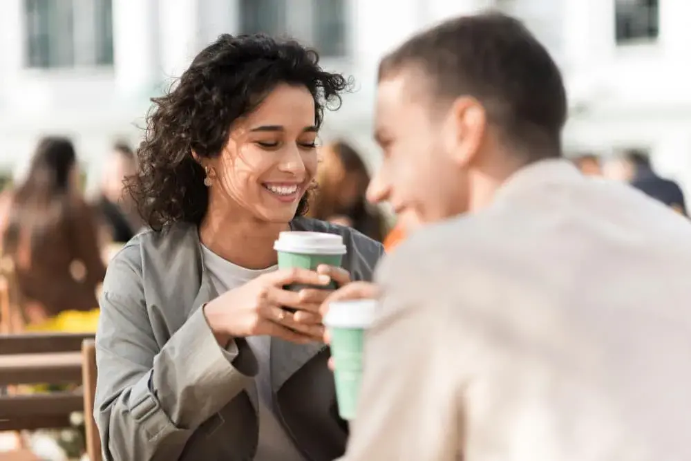 A smiling couple sits outdoors at a café, enjoying coffee and conversation on a sunny day. The image conveys ease and connection, symbolizing the peace of mind and financial freedom possible through cash-out refinancing with Chris Lewis Home Loans.