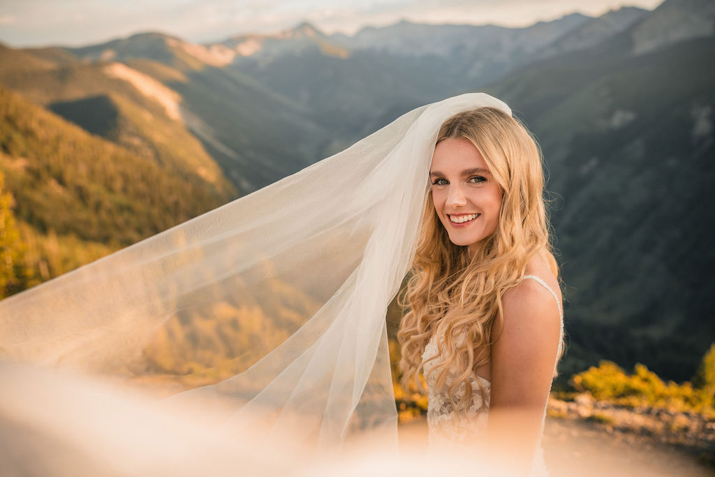 Bride smiling beneath a flowing veil with mountains behind her