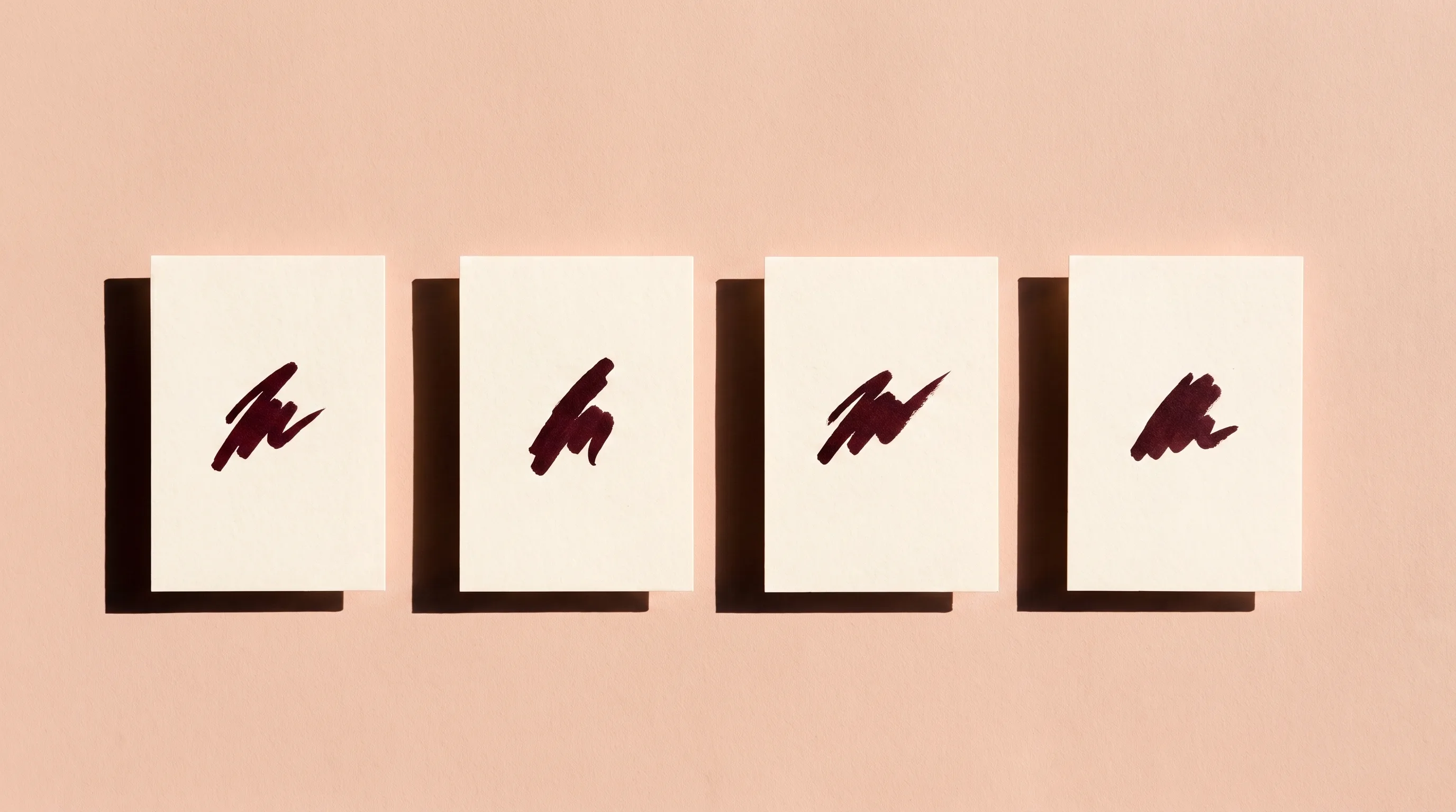 Four cream cards in a single row, each carrying one short ink mark, lit hard from the left
