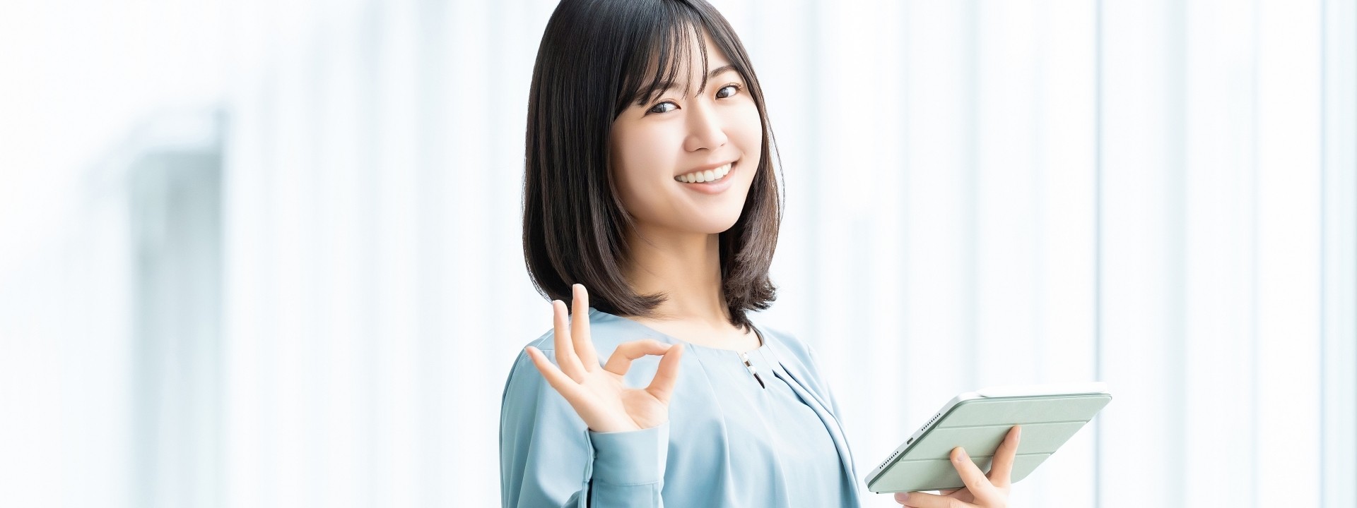 女性がタブレットを持ちながらOKサインをしているビジネスシーンの画像