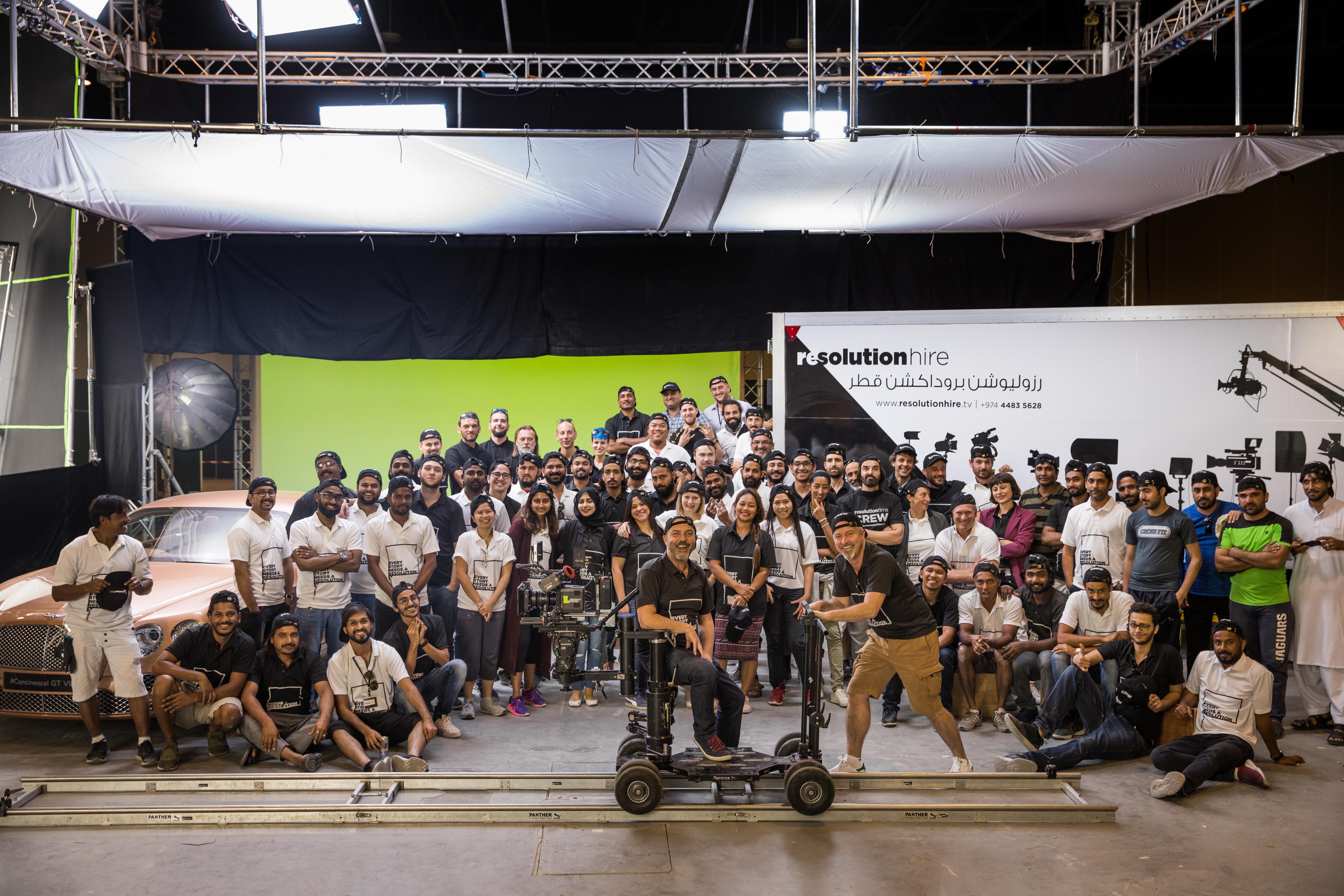 A large group photo of diverse team members gathered in an industrial-style space with arched ceiling.