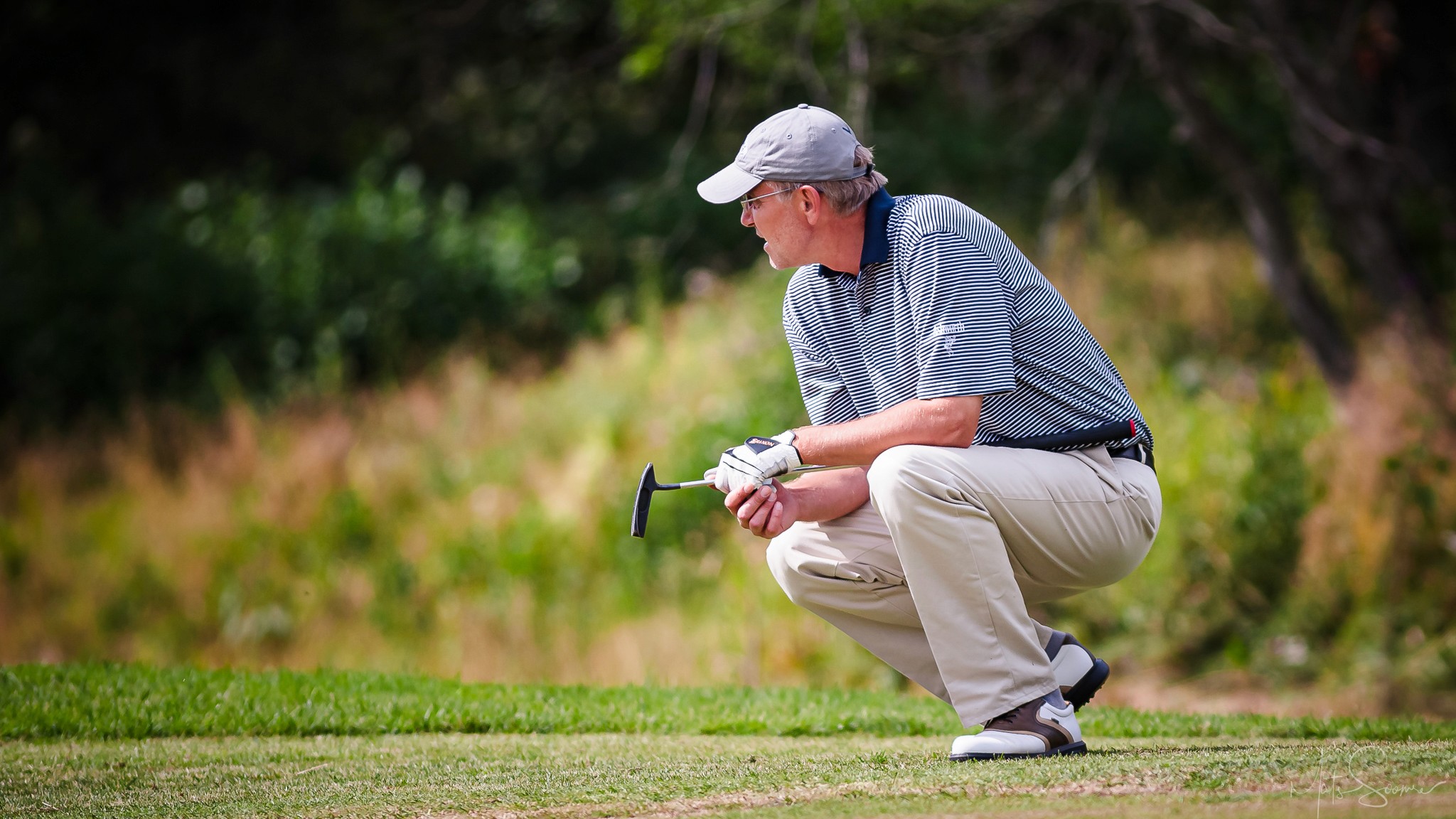 Golfer in striped shirt crouches to read a green, putter in hand. Photographed by Mats Soomre, 2007.