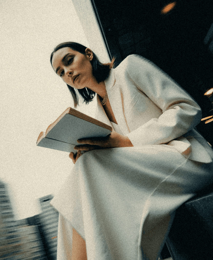 woman in a white suit sitting in te downtown of a city with a book in her hands