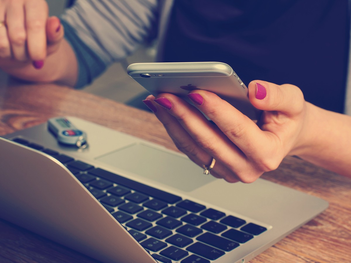 A lady holding an iPhone while using her MacBook