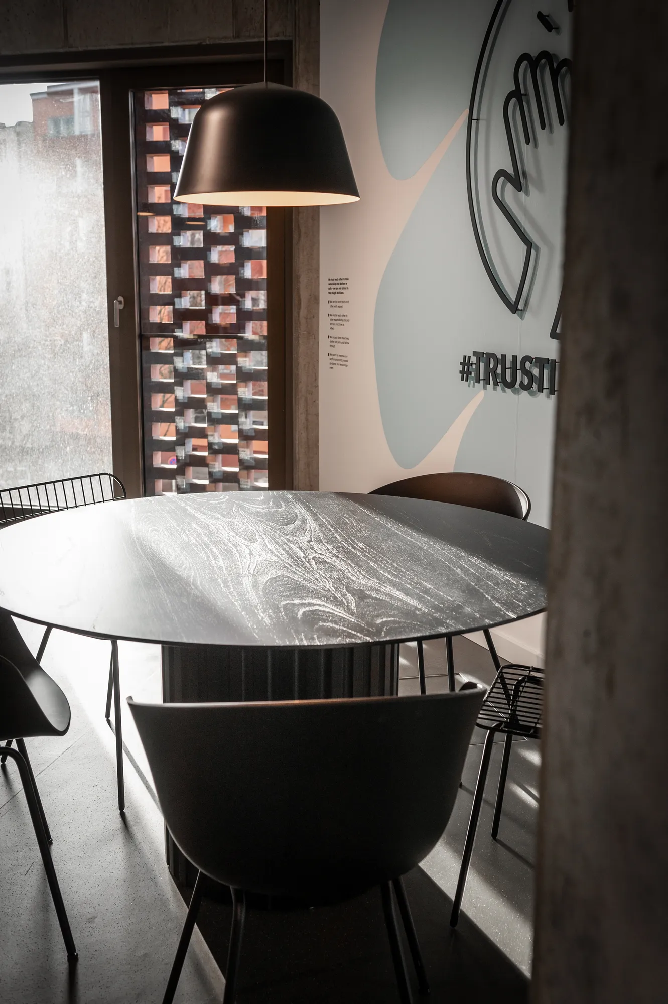 Meeting room with lilac wall, wooden panelling, round table with pink chairs and a screen.