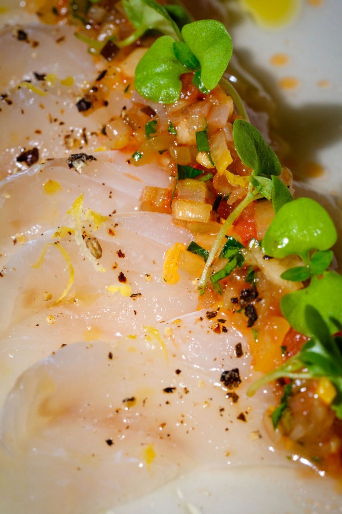 Close-up of a crudo dish topped with diced vegetables, herbs, and citrus zest.