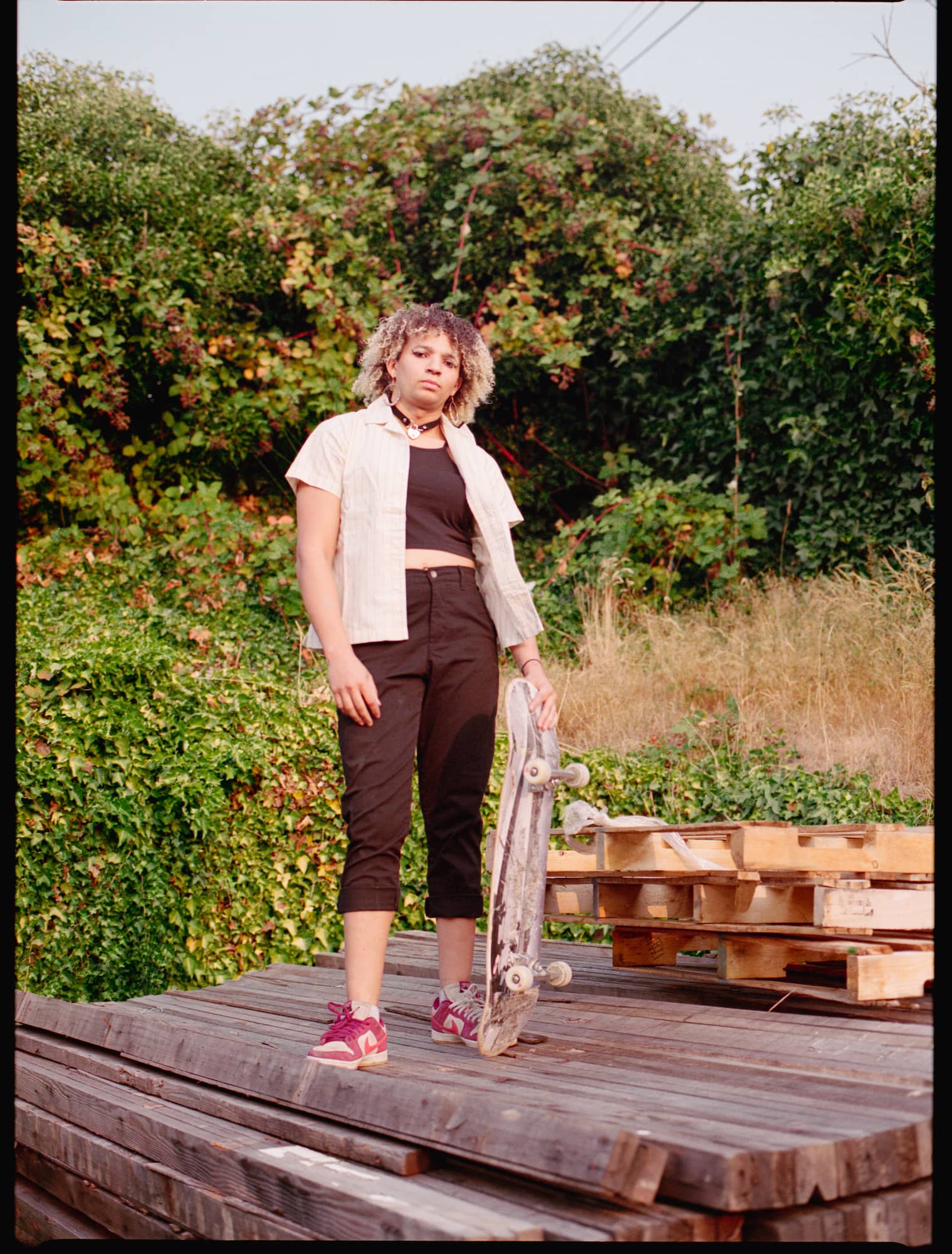 A woman on a wooden platform poses with a skateboard, showcasing her skating gear.