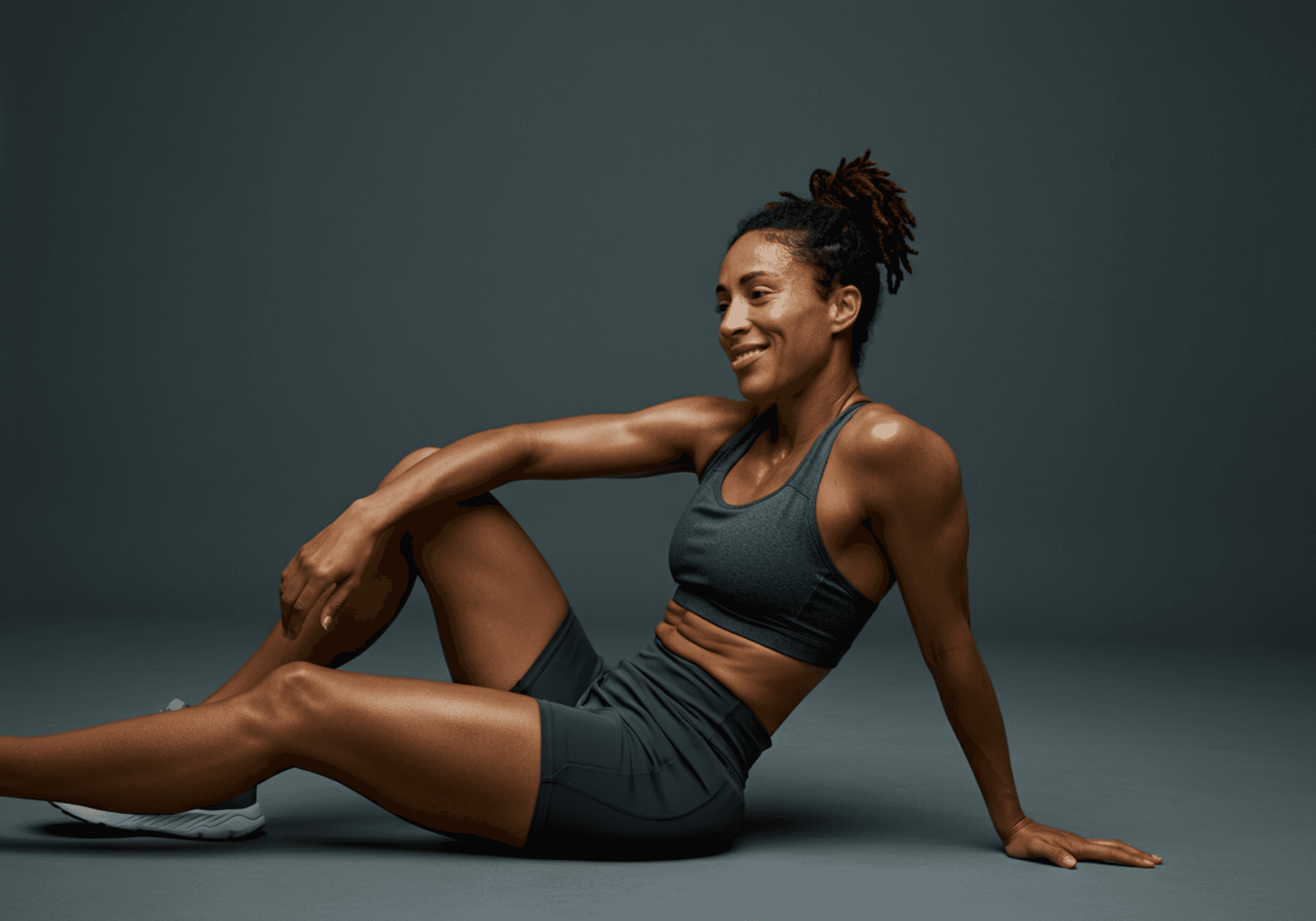 Fit female athlete resting post-workout, smiling with confidence—highlighting strength, recovery, and the results of consistent physical therapy and training.
