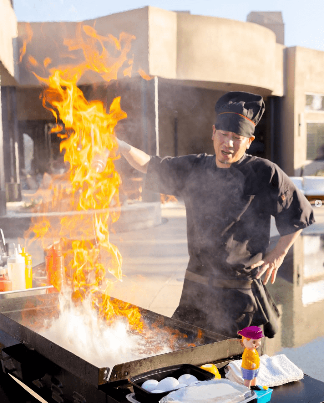 An overhead shot of Patatas Bravas or seasoned roasted potatoes, drizzled with a creamy white aioli sauce and sprinkled with chives, served on a dark gray plate alongside a small bowl of spicy red sauce.