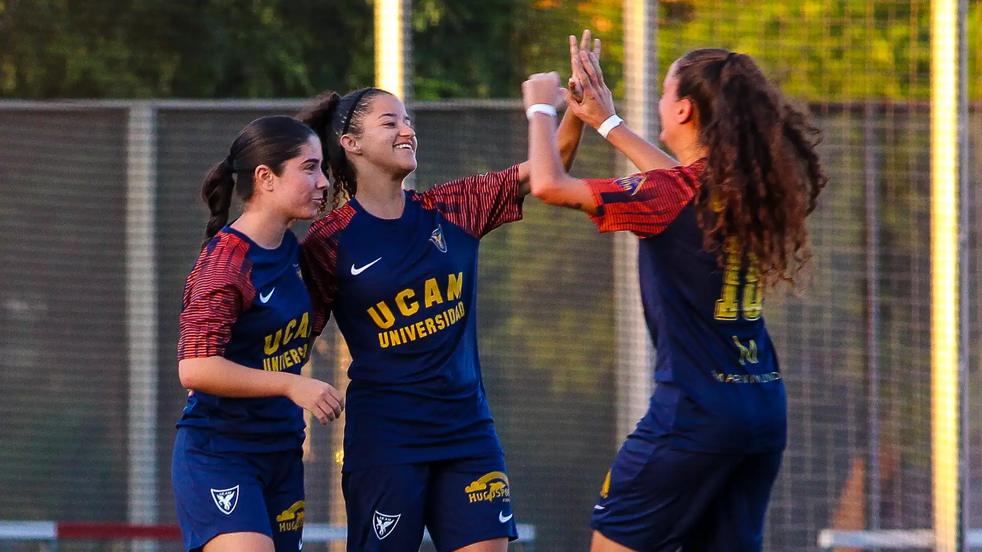 Jugadoras del UCAM International Football Team femenino celebrando un gol con gesto de victoria durante un partido universitario | UCAM Universidad Católica de Murcia