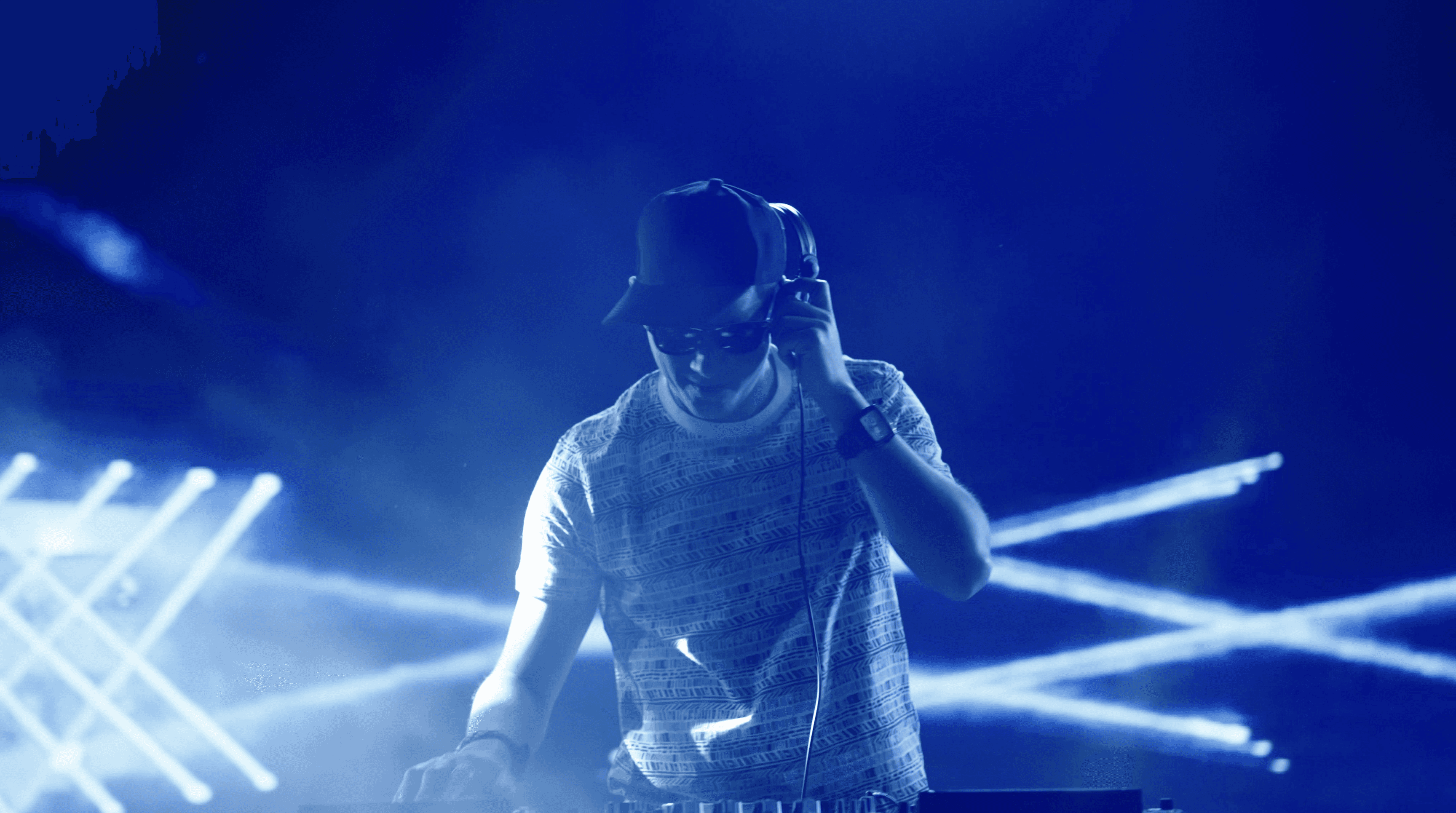 Live DJ set on stage — performer at the decks under dramatic blue stage lighting with moving beam effects