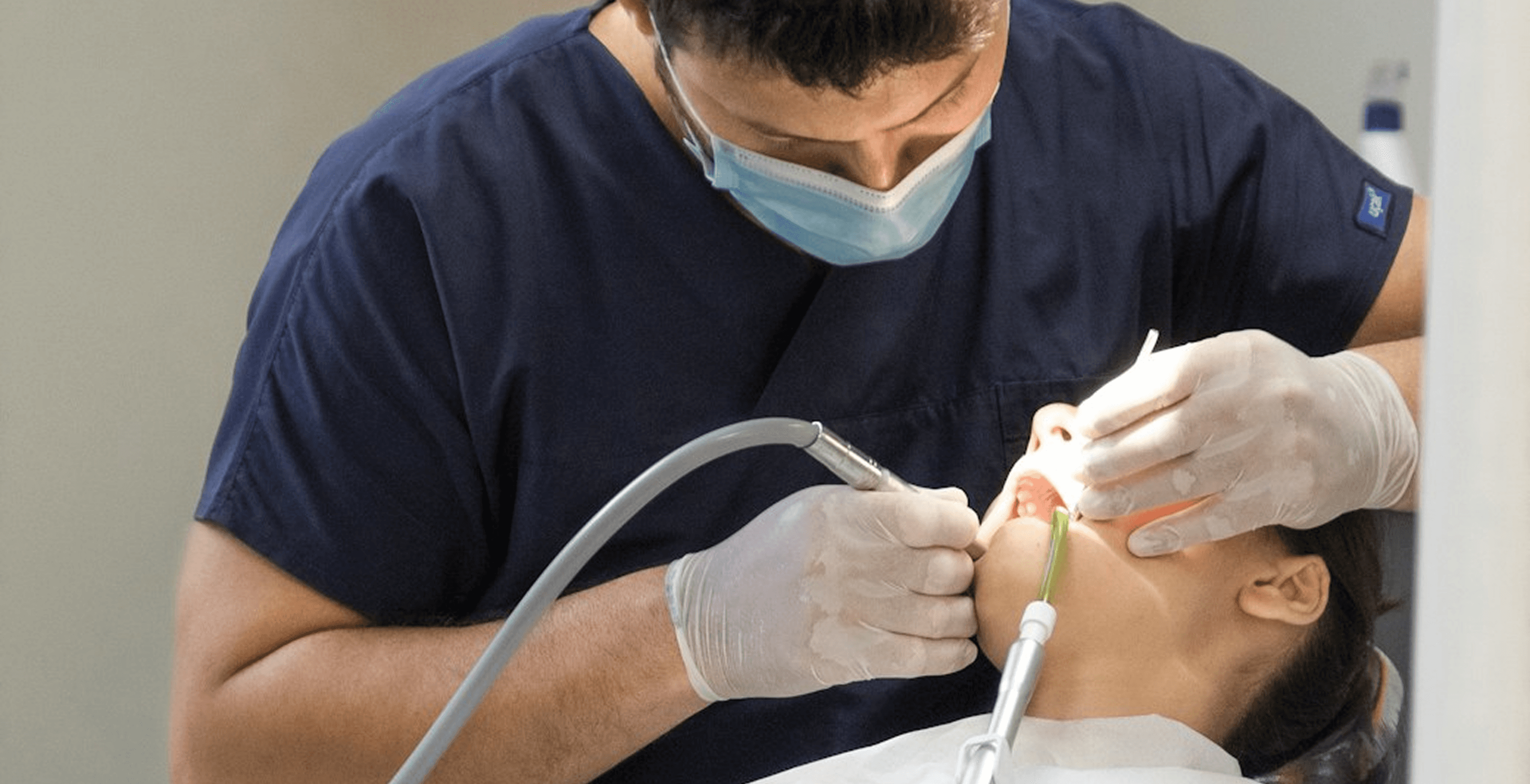 Dental professional performing procedure on patient using instruments and suction in clinic setting.
