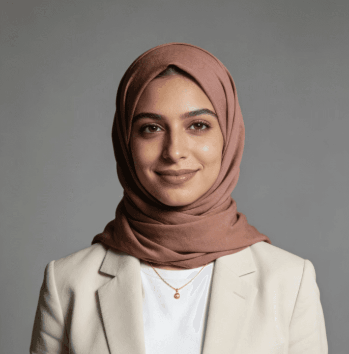 A professional portrait of a woman in a beige blazer and pink hijab