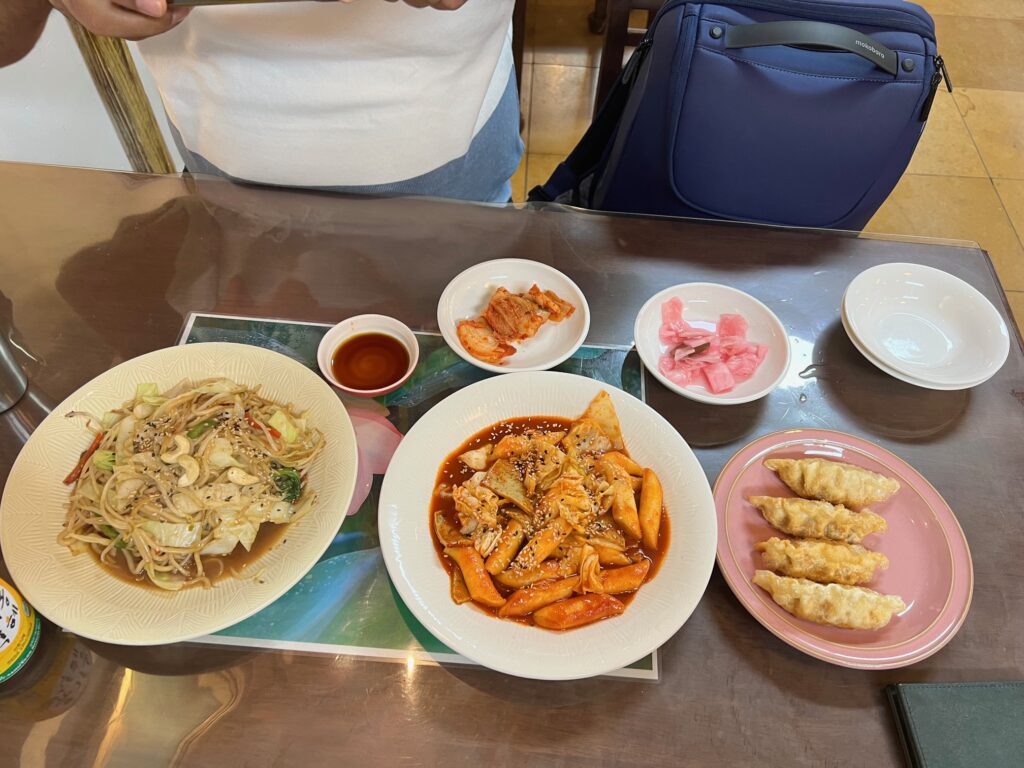 Stir fried noodles, tteobeoki, and fried dumplings along with kimchi are served on a table.