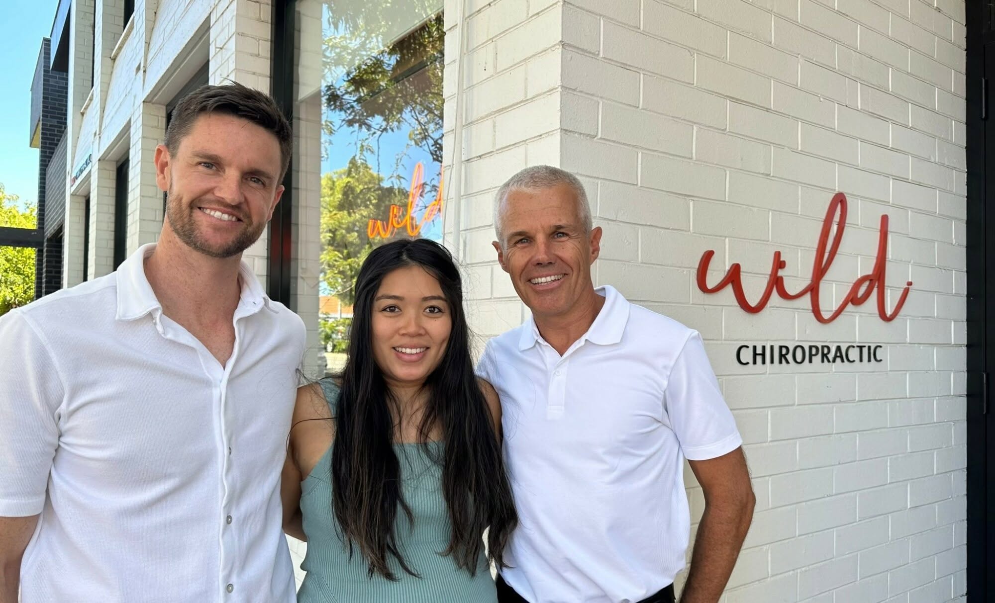 Three people outside the Wild Chiropractic practice beside its wall signage
