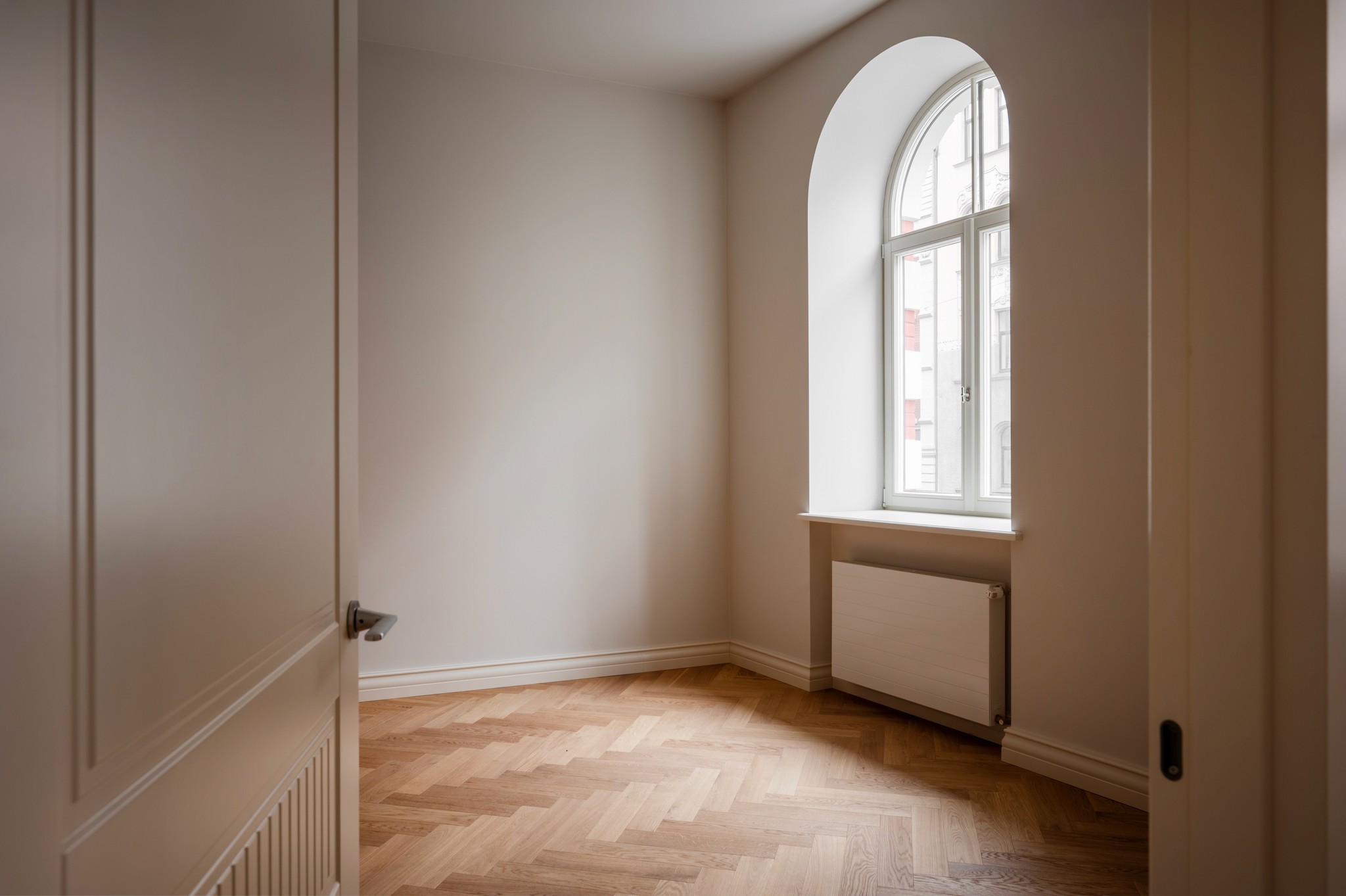 Bright, airy interior with arched doorways, wooden furniture, and a view of greenery outside.