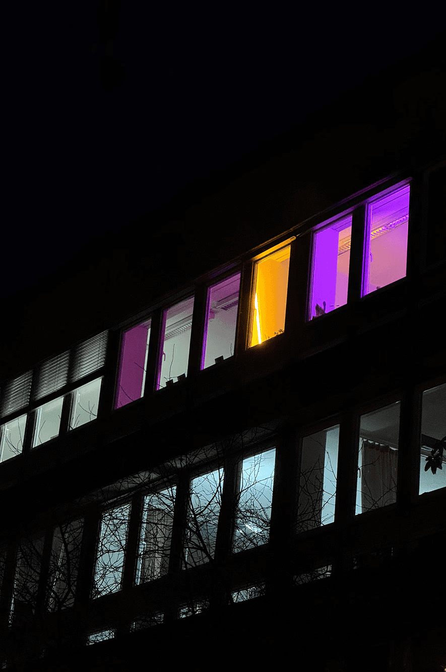A woman wearing headphones and a black sports bra is DJing at a mixing console, with shelves containing white items and a single black item in the background, showcasing her unique branding style.