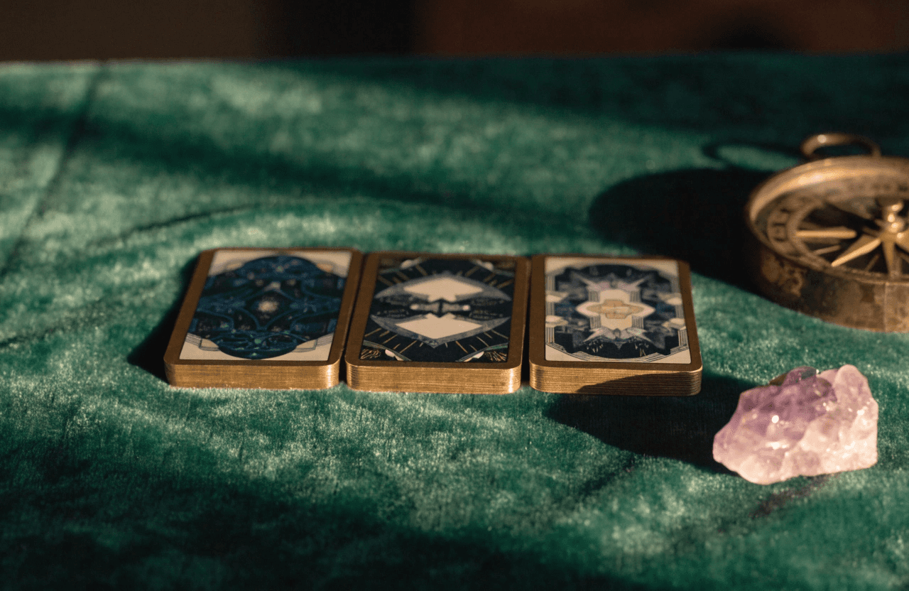 A realistic macro photograph of three Tarot cards laid out in a clean alignment on a rich #2E4032 Mossy Green velvet cloth. Beside the cards rests a raw, polished amethyst crystal and an ancient #8C7D64 Aged Bronze compass.