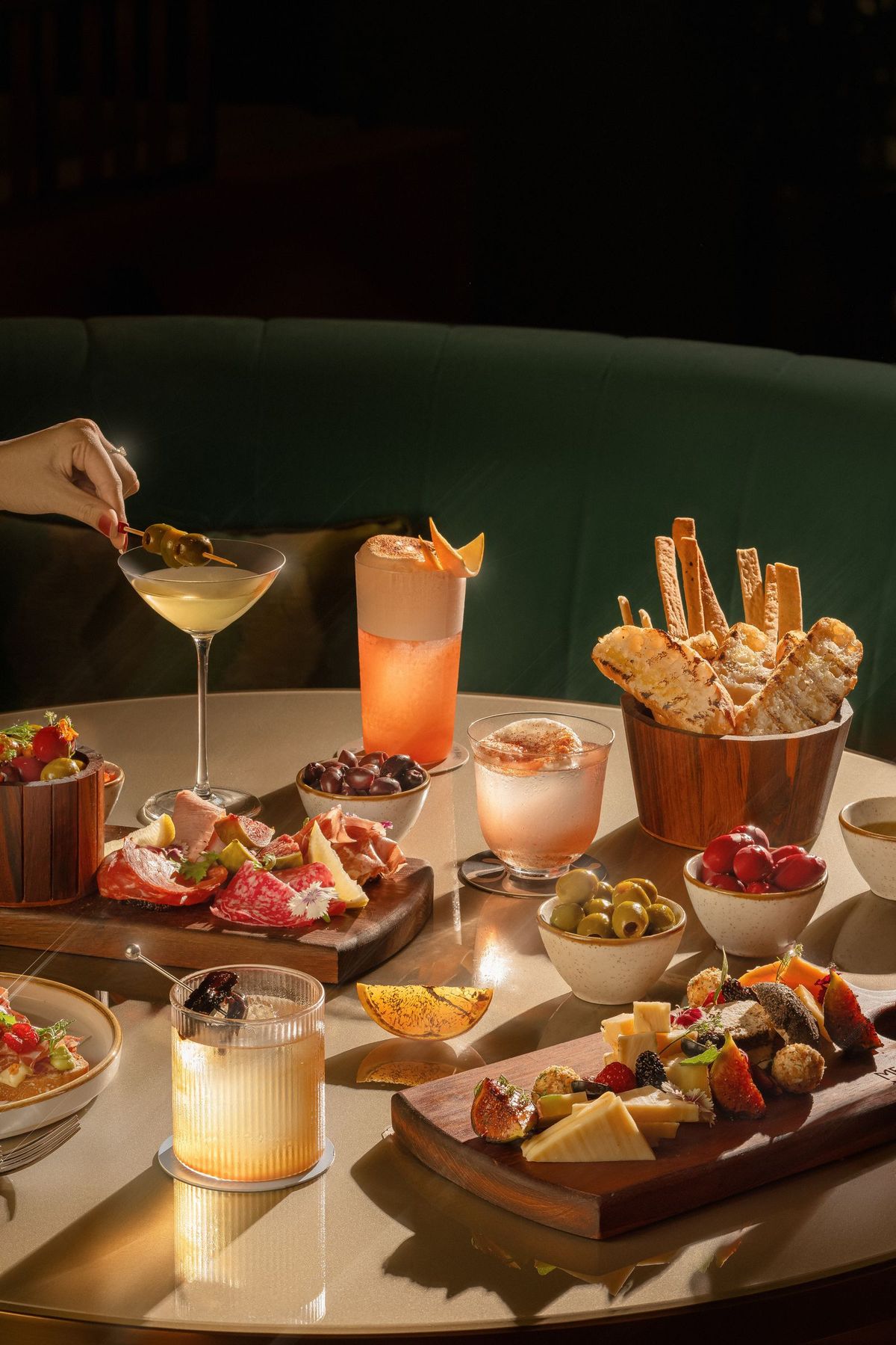 Elegant table of small plates, charcuterie boards, olives, and signature cocktails at Dhoom, emphasizing sophisticated plating and ambiance.