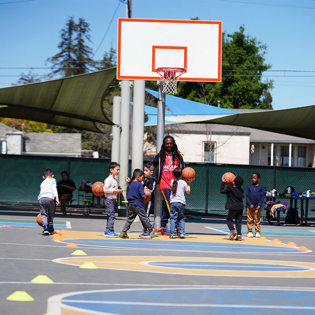 children practicing basketball drills with a coach during an outdoor sports enrichment activity at school